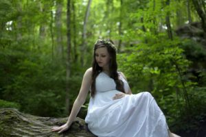 pregnant girl in white dress sitting on fallen tree